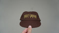 Front view of the brown Discovery hat with yellow lettering and detailing